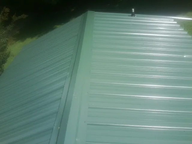 New green metal panels meeting at the ridge of a roof — Flat Roof Repair work by our crew in Meridian