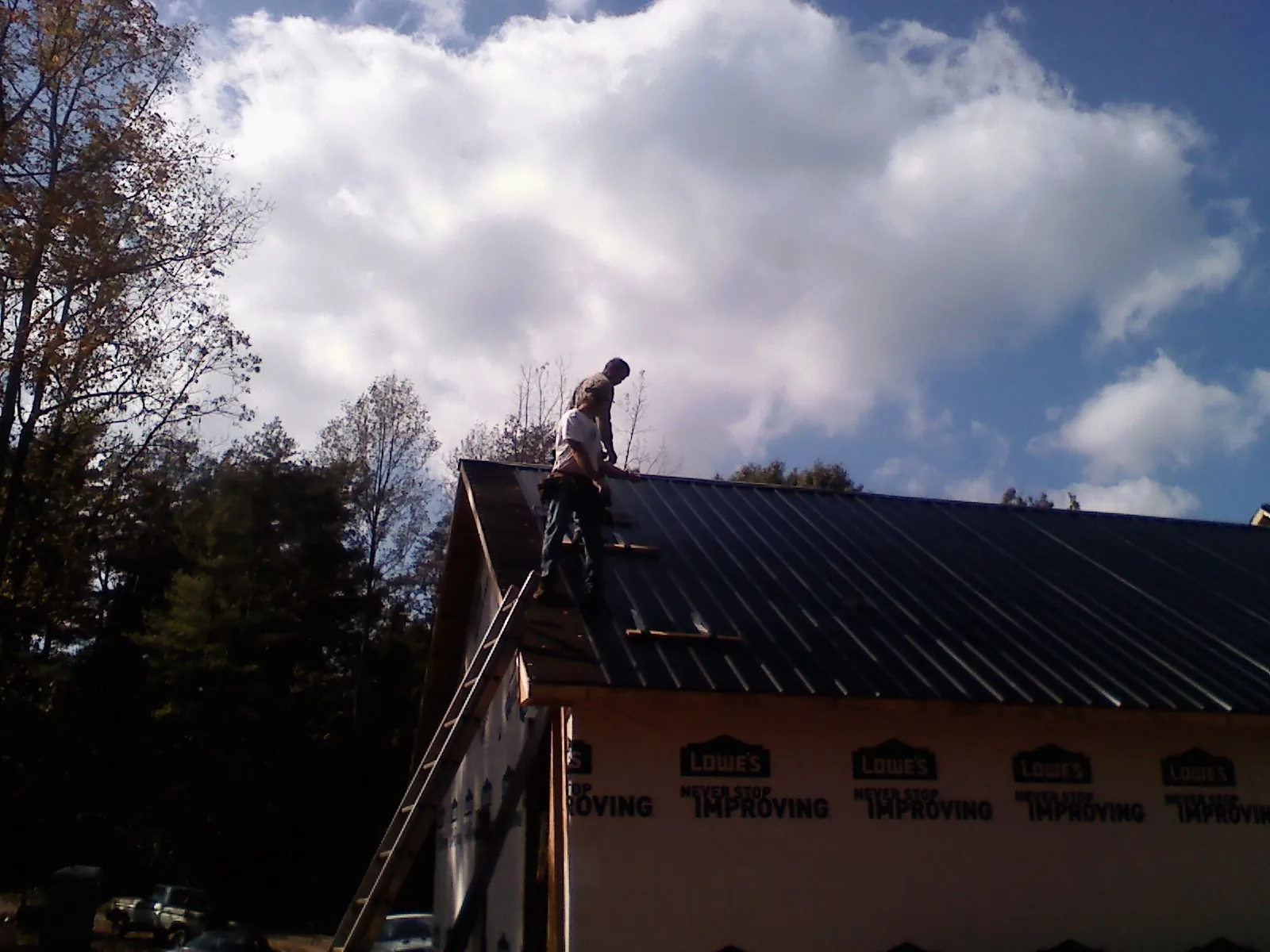 Roofer fastening dark metal panels high against a cloudy sky, from a Roof Inspection job in Meridian