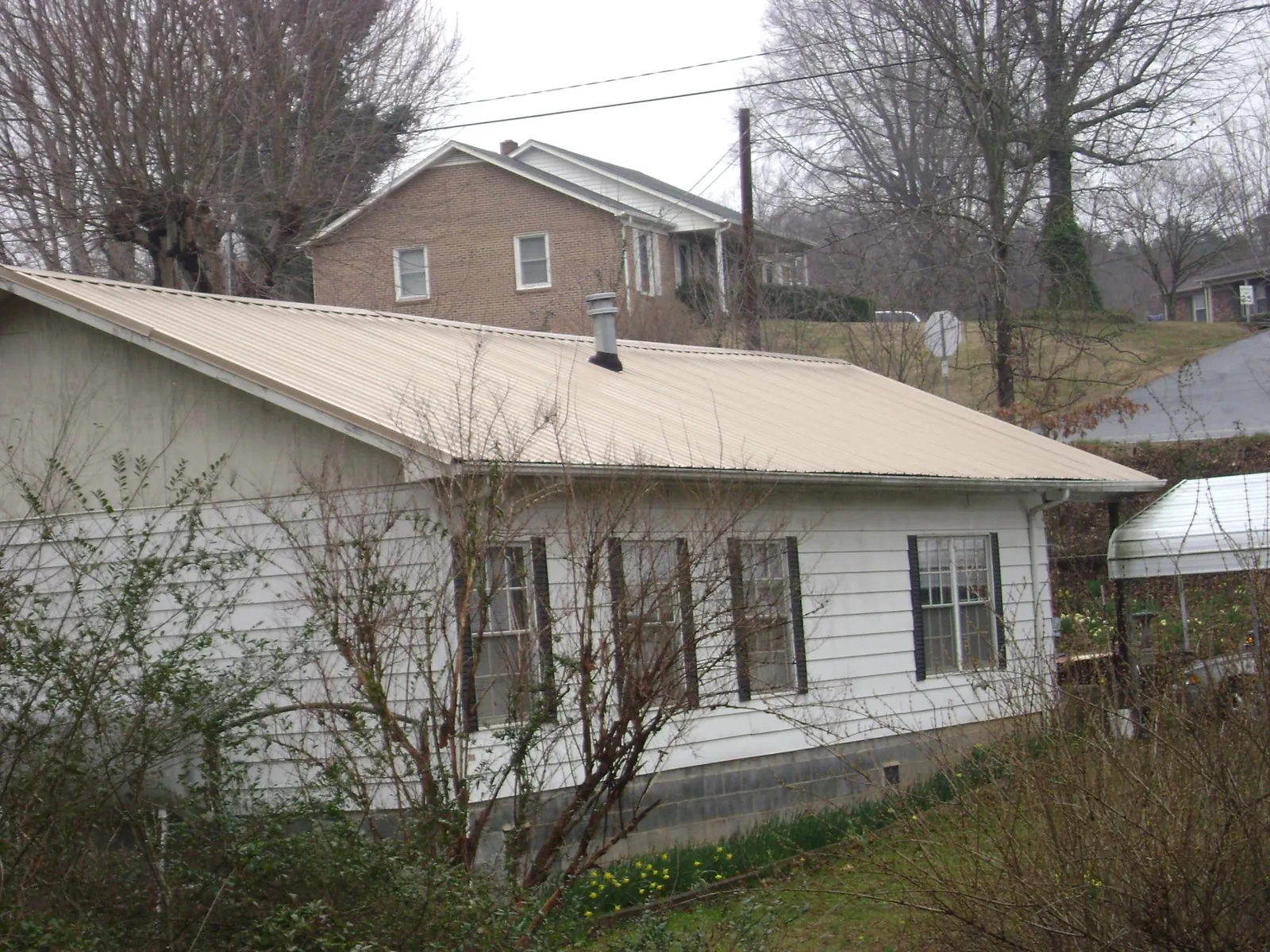 Tan metal roof on a white sided house set into a hillside — Commercial Roofing by Roofing Brothers in Meridian